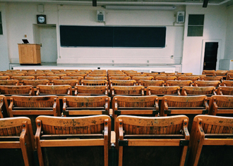 Ein leerer Klassenraum an einer Hochschule mit Blick von der hintersten Reihe aus zur Tafel hin. 